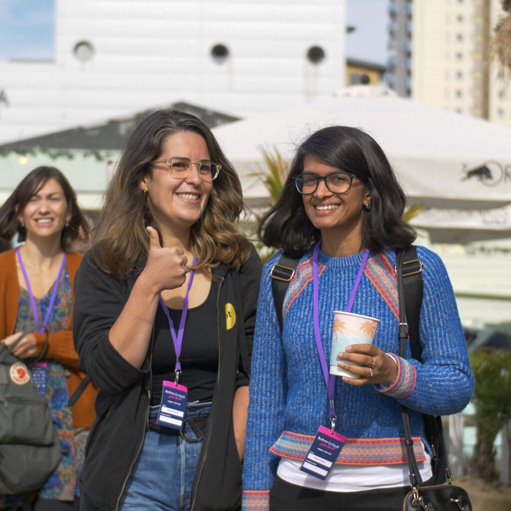 Two smiling women walking in the sunshine, outdoors at the HalfStack and CityJS: At the Beach event in London, September 2021.